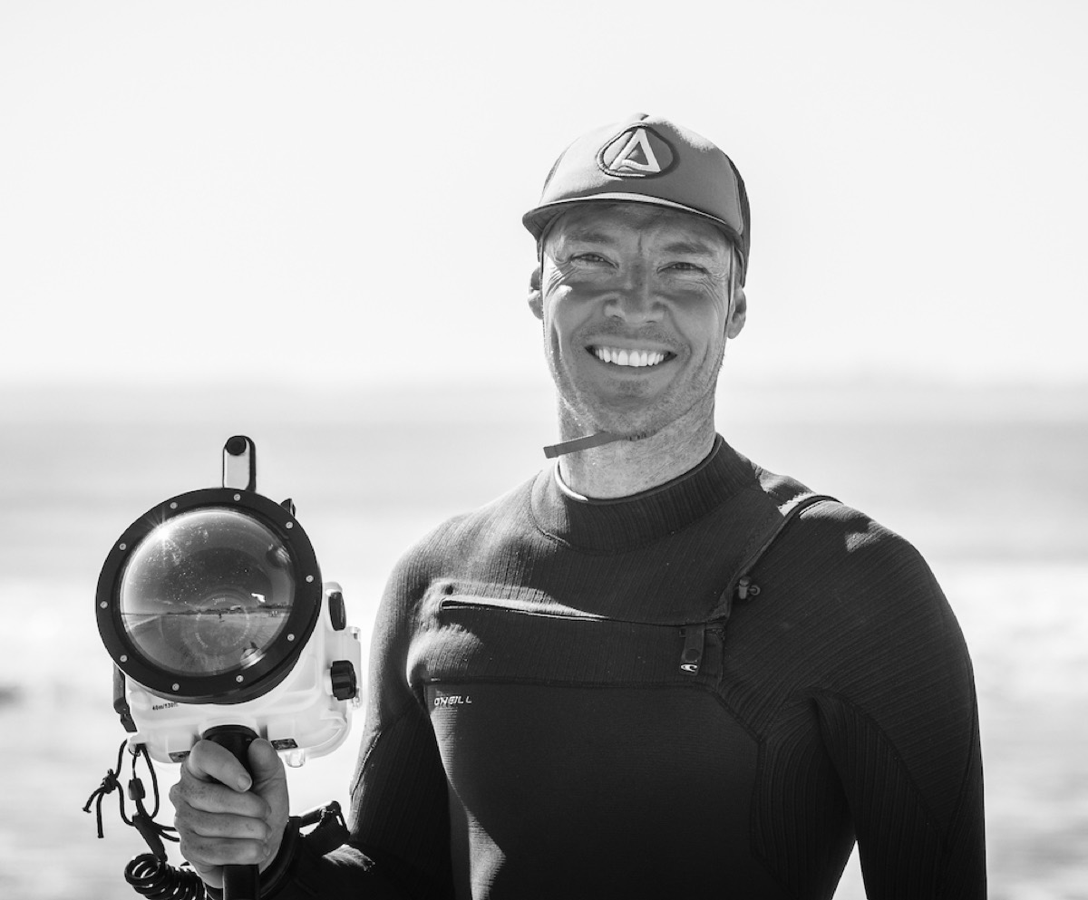 Bradley Hook in a wetsuit and cap holding a water-camera housing, ready to shoot from the water