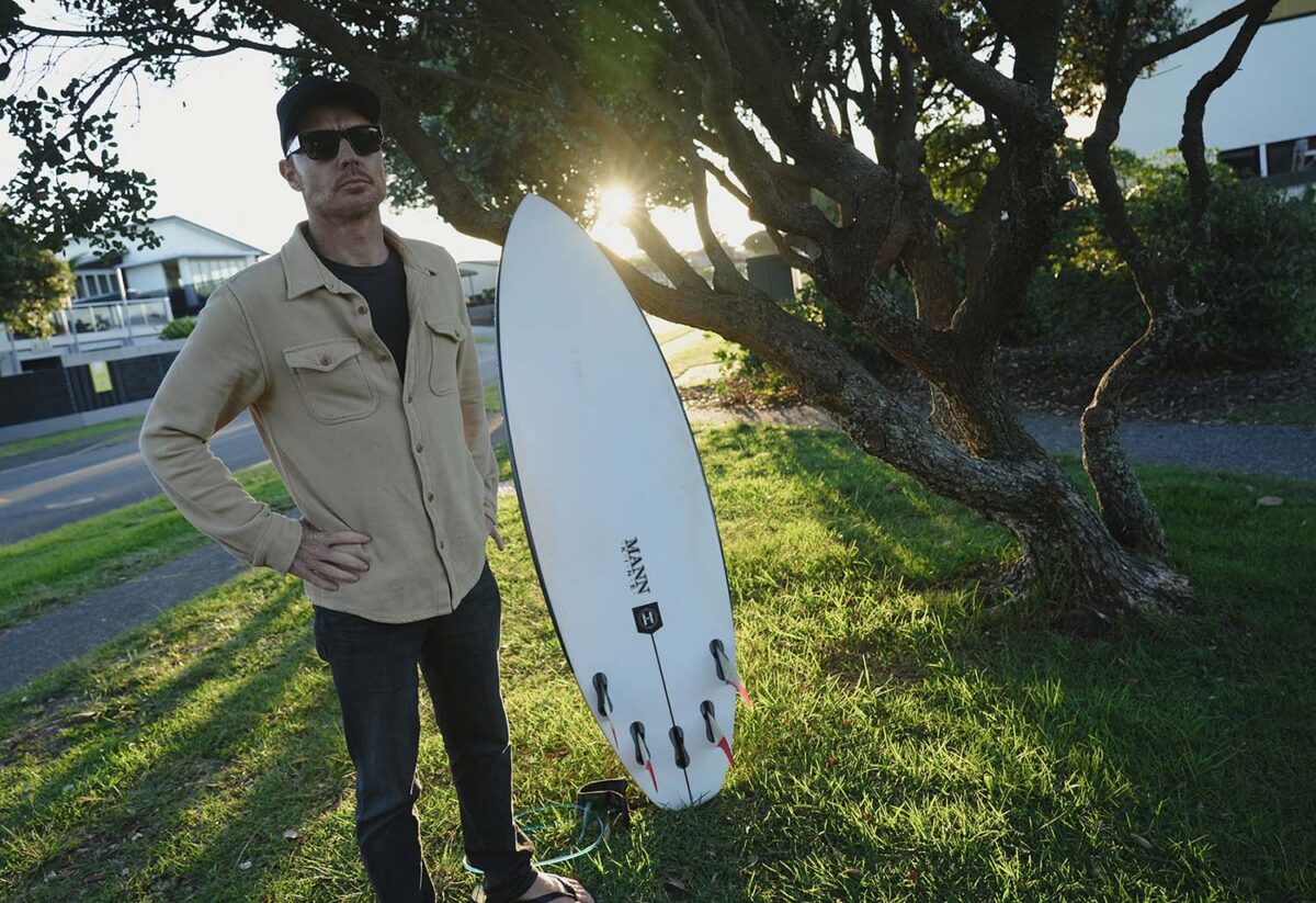 A surfer standing next to his surfboard by Firewire, Slater Designs – image
